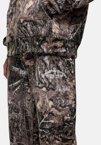 Camo-patterned joggers in brown and gray tones with a soft texture. Features white "Good For Nothing" logo on the lower leg.