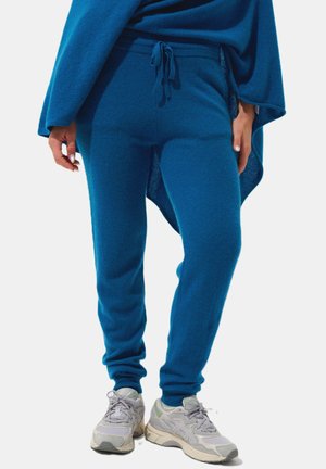 Jogging blu nonni con fascia elastica in vita e lacci. Tessuto morbido e gambe affusolate. Abbinati a scarpe da ginnastica grigio chiaro.