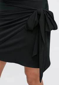 Czarna spódnica z detalem w formie skręconego węzła, wykonana z teksturowanej tkaniny o gładkim wykończeniu, z asymetrycznym dołem.