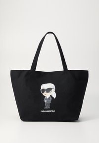 Black tote bag made of canvas featuring a graphic of a cartoon figure in sunglasses and a suit, with "KARL LAGERFELD" printed below.