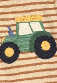 Zielony haftowany traktor na paskowanym beżowo-brązowym tle. Traktor ma żółte akcenty i niebieski szczegół wydechu.