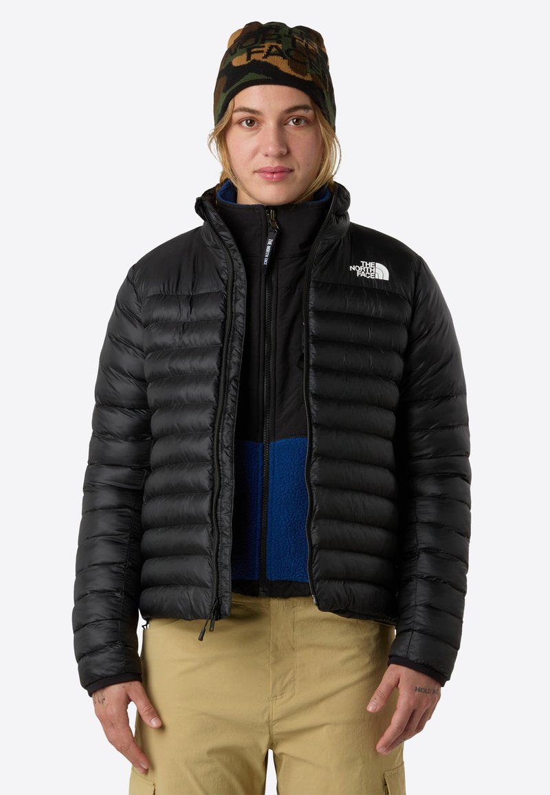 Juodas pūkinis švarkas su horizontaliomis siūlėmis, užtrauktuko priekyje ir "The North Face" logotipu. Dėvimas virš mėlynos fliso striukės ir smėlio spalvos kelnių. Kamufliažinė kepurė.