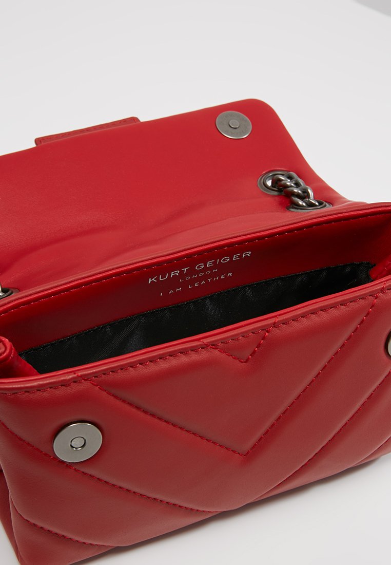 Czerwona skórzana torebka z haftowanym wzorem w zygzak, srebrnymi akcentami, zapięciem na zatrzask i czarną podszewką. Etykieta głosi "Kurt Geiger, jestem skórą."