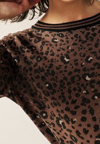 Brązowy sweter w cętki z nadrukiem leopardzim, z prążkowanym dekoltem i ciemnymi paskami. Miękka struktura z delikatnym połyskiem w całym materiale.
