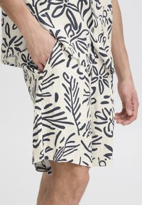 Cream shorts with a navy leaf pattern, featuring side pockets and a relaxed fit. Material appears lightweight and breathable.