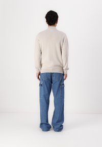 Hellbeige Strickpullover mit hohem Kragen und gerippten Bündchen, kombiniert mit lockeren blauen Denim-Cargo-Hosen mit seitlichen Taschen.