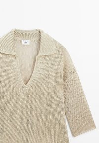 Beige gebreide pullover met een V-hals en brede kraag. Beschikt over driekwartmouwen en een losse weefstructuur. Label zichtbaar bij de halslijn.