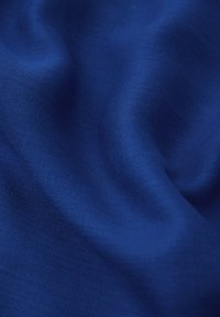 Královská modrá látka s hladkým texturovaným povrchem, vykazující jemné variace světla a stínu přes její záhyby.