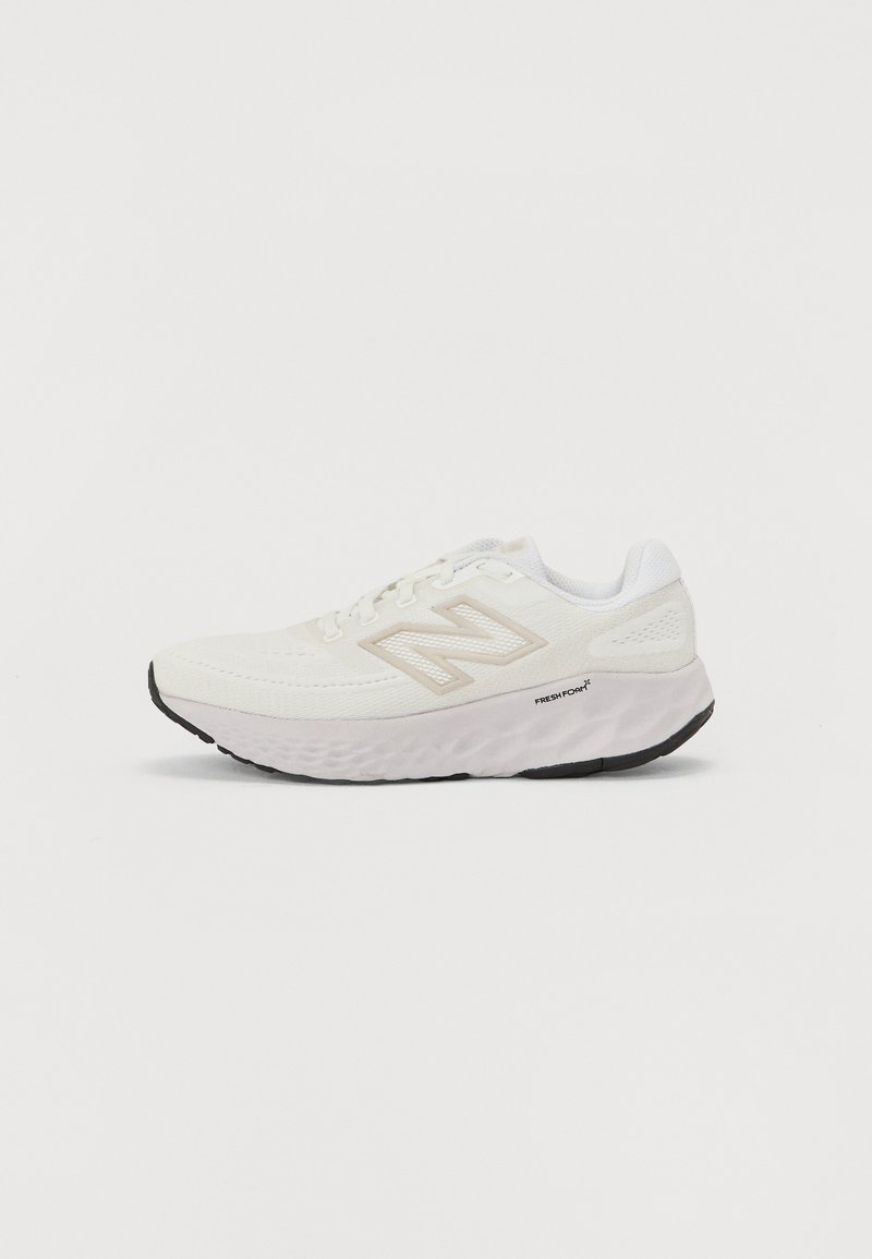 Bijela Atletska cipela s mrežastim gornjim dijelom, podstavljenim ovratnikom i debelim teksturiranim potplatom. Ima svijetlosivu oznaku i "New Balance" logo sa strane.