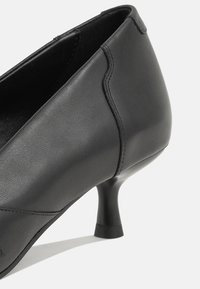 Escarpin femme en cuir noir avec un bout rond et un petit talon bas évasé, vu de l'arrière de côté.