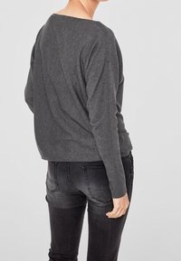Grijze gebreide trui met een relaxte pasvorm, brede halslijn en lange mouwen, gecombineerd met donkerdenim jeans met achterzakken.