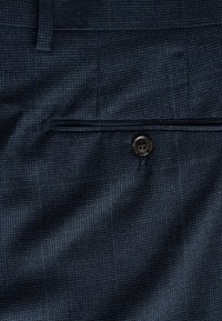 Temno modro tkanino z rahlim karo vzorcem, ki ima zapiranje na en gumb in raven sprednji žep.