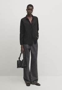 Chemise noire en lin à boutons, jean gris à jambes larges, sac noir avec poignées nouées et sandales noires. Coupe simple et décontractée.