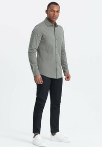 Langarm, hellgrünes Hemd mit Button-Down-Kragen und Brustlogo, kombiniert mit dunklen Jeans und weißen Sneakern. Sanfte Stofftextur.