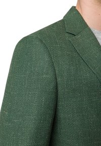 Zielony żakiet w wzór rybiej ości z teksturowanej tkaniny. Posiada klapy w kształcie notcha oraz wyraźną konstrukcję ramion. Zbliżenie ukazujące szczegóły materiału.