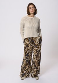 Un pull tricoté de couleur beige clair avec une coupe ample. Un pantalon à jambe large avec un imprimé animal à pois dans des tons de marron, noir et beige.
