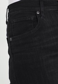 Jeans de denim negro con una textura suave, con un bolsillo frontal, botón plateado y costuras a lo largo de las costuras. Diseño moderno de corte slim.
