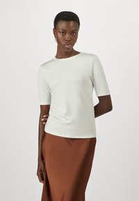 Top aderente grigio chiaro con maniche corte e scollo rotondo, abbinato a una gonna marrone. Tessuto liscio, design minimale.