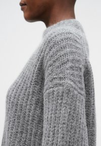 Vue de profil d'une personne portant un pull en maille gris doux et épais avec un motif texturé et un col rond montant.