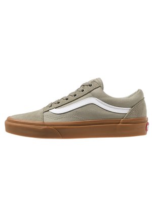 Beige lage sneaker van canvas met een witte zijstreep, bruine rubberen zool, veterlijke sluiting aan de voorkant en gevoerde kraag, getoond in zijaanzicht.