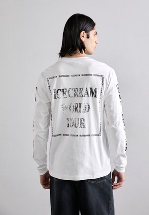 Chemise blanche à manches longues avec des graphismes en texte noir, incluant "ICECREAM WORLD TOUR", avec une impression texturée contrastante et une coupe décontractée.