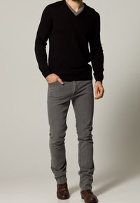 Maglione nero a scollo a V con colletto interno grigio, abbinato a jeans grigi aderenti e scarpe marroni. Il maglione presenta polsini e orlo a coste.