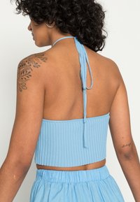 Top cropped canelado azul claro com atadura ao pescoço, apresentando uma textura suave e um design ajustado. Inclui detalhe de faixa elástica.