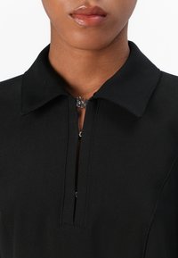 Black collar top featuring a front zipper with a silver pull, smooth fabric, and structured neckline. Close-up of the upper chest area.