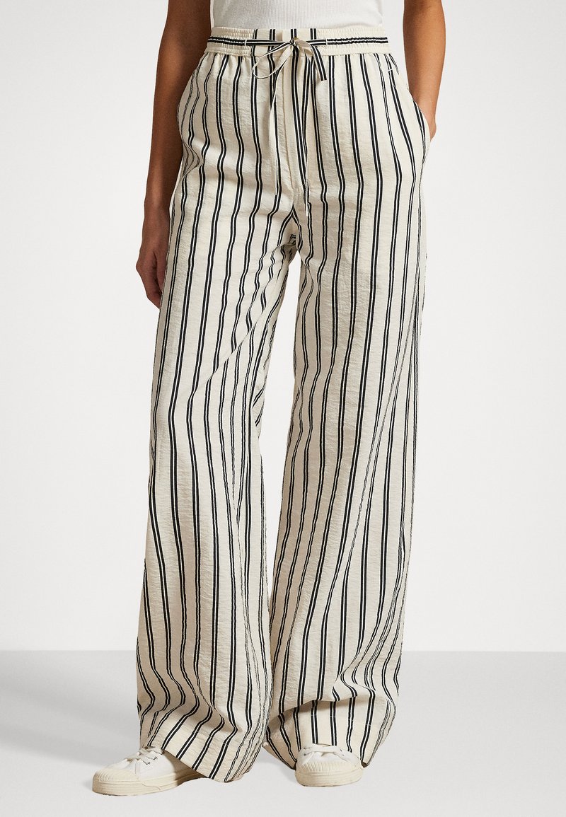 Pantalons larges légers de couleur crème avec des rayures verticales navy. Dotés d'une taille avec un cordon de serrage et de poches latérales. Texture douce.