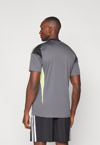 T-shirt de sport gris avec épaules noires et accents verts fluorescents, fabriqué en tissu léger. Conçu pour le confort, associé à un short noir.