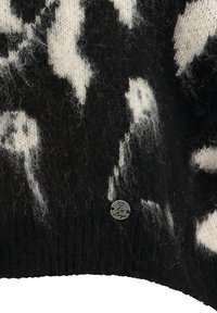 Sweter z dzianiny w czarno-białym wzorze, o miękkiej teksturze, z małą okrągłą metalową metką z sercem na dole.