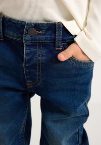 Jeans di denim in blu scuro con cuciture arancioni a contrasto, dotati di tasca frontale, chiusura con bottone e vestibilità rilassata.