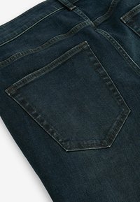 Jeans de mezclilla oscura con un gran bolsillo trasero rectangular con una textura sutil. La tela tiene un ligero brillo y costuras visibles.