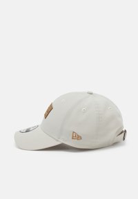 White baseball cap made of cotton with brass hardware, featuring a round logo patch, side embroidery, and adjustable strap at the back.