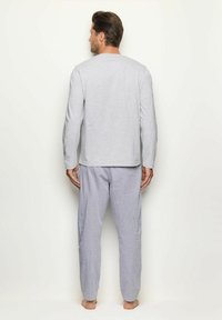 Camisa de manga larga gris con cuello redondo combinada con pantalones de pijama a rayas azules y blancas, hechos de tela suave, con un corte holgado.