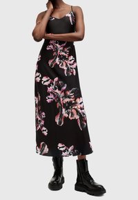 Svart blomstermaxiklänning med rosa och vita bladmönster, justerbara tunna axelband, slät tyg, kombinerad med svarta kängor.