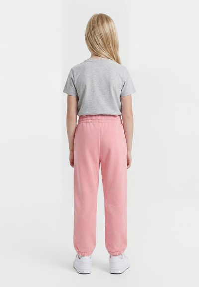 Hosszú szőke hajú gyermek háttal áll, szürke rövid ujjú pólót, rózsaszín elasztikus derékú nadrágot és fehér tornacipőt visel.