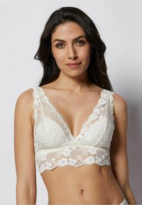 Bralette en dentelle de couleur blanc cassé, avec un décolleté V profond et de larges bretelles en dentelle. Des motifs floraux ornent la dentelle et l'ourlet, ajoutant texture et détail.