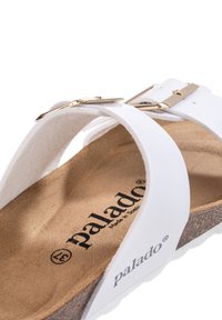 Sandalo bianco con suola in sughero, design piatto e due cinturini regolabili con fibbia dorata. La soletta presenta una finitura morbida e testurizzata.