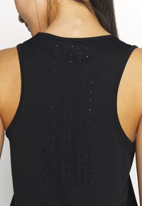 Mustavitsi, jossa on sileä pinta ja vaakasuoria sekä pystysuoria reikiä ilmanvaihtoa varten. Spaghetti-henkärit asettuvat olkapäille.