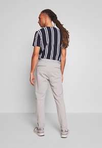 Camiseta de rayas azul marino de manga corta, combinada con pantalones gris claro y zapatillas grises. Conjunto casual, mostrando vista trasera.