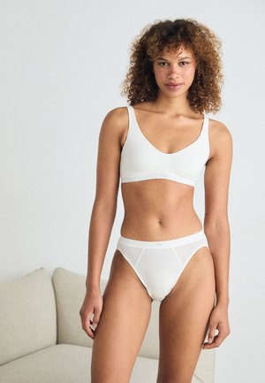 Bijela ćebasta bralette i gaćice set s glatkom teksturom, podesivim trakama i minimalističkim dizajnom, s diskretnim logotipom marke na pojasu.