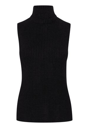 Femme portant une robe à imprimé léopard à manches longues, un pull sans manches noir, des collants noirs transparents et des bottines noires, debout avec les bras croisés.