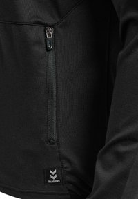 Top sport negru, cu un material texturat, o buzunar cu fermoar pe partea stângă și un label cu logo la tiv.