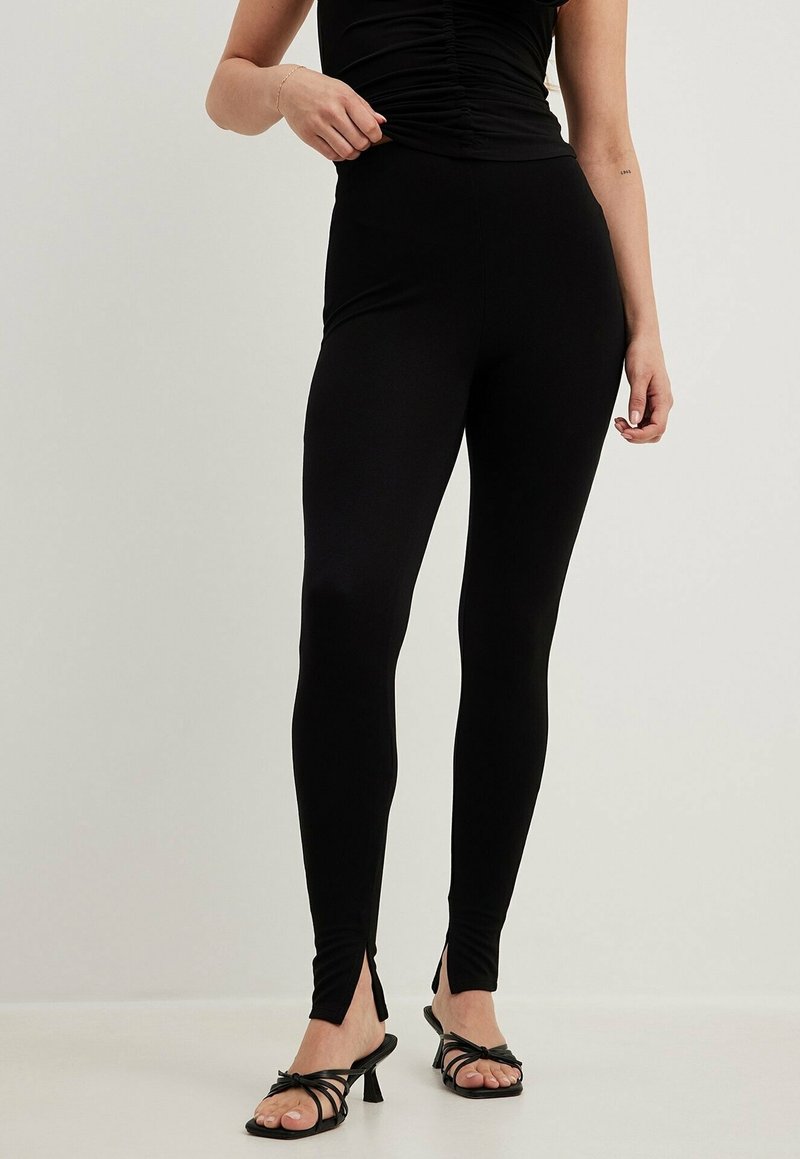 Svarta leggings i stretchigt material, med en åtsittande passform och unika springor vid anklarna, i kombination med svarta klackskor medremmar.