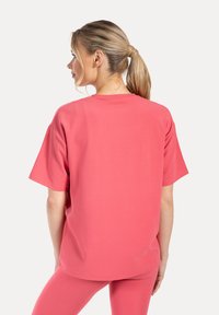 T-shirt a maniche corte realizzata in tessuto liscio ed elastico di un rosa acceso, con collo rotondo e vestibilità morbida, dettagli di cuciture a vista.