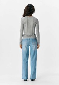 Grå langærmet skjorte kombineret med lyseblå lige ben jeans. Jeansene har to baglommer og en falmet vaskestruktur.
