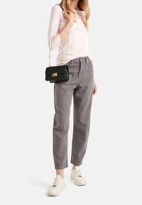 Růžovo-bíle pruhovaný dlouhý rukáv, šedé kalhoty s vysokým pasem, černá kabelka přes rameno se zlatými detaily a bílé tenisky.