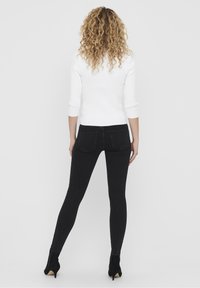 Jeans skinnies negros de tiro alto con una textura suave, bolsillos traseros y una silueta ajustada, combinados con una blusa blanca de manga tres cuartos acanalada.