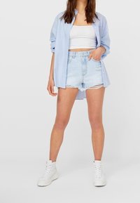 Szorty dżinsowe w jasnym odcieniu z postrzępionym dołem, zestawione z dopasowanym, białym topem na krótko oraz luźną, jasnoniebieską koszulą na guziki. Białe sneakersy za kostkę.